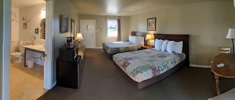 A hotel room with two beds, a bathroom, a desk, and a dining table.
