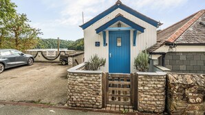 Un petit bâtiment d’un seul étage, avec une porte bleue et une entrée surmontée d’un mur en pierre.