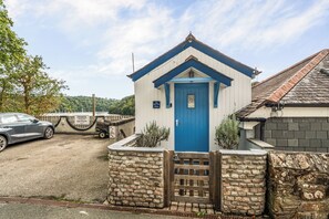 A small, single-story building with a blue door and a stone wall entrance. - 1 Bed Cottage - Sleeps 2 - Wifi (Truro)