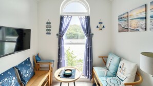 Une pièce avec un téléviseur, un canapé, un fauteuil, une petite table et une fenêtre avec des rideaux.