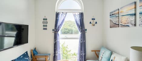 A room with a TV, a sofa, a chair, a small table, and a window with curtains.