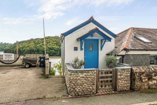 A small, single-story building with a blue door and a sign indicating it is a private parking area for Rose Cottage.