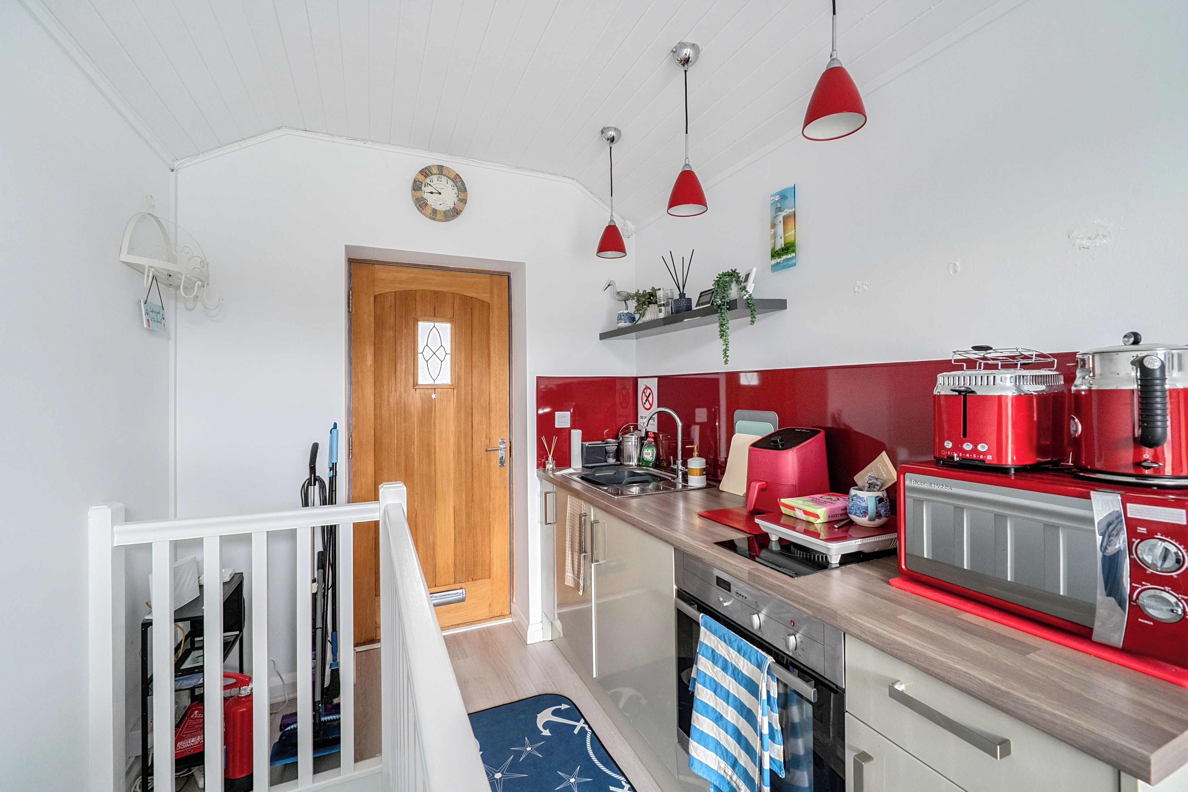 A modern kitchen with red appliances, a wooden door, and pendant lights.