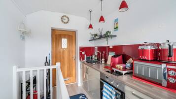 A modern kitchen with red appliances, a wooden door, and pendant lights.