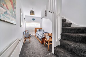 A bedroom with a bed, a chair, a table, a window with blinds, a clock, and a staircase. - 1 Bed Cottage - Sleeps 2 - Wifi (Truro)