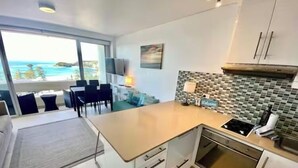 Een moderne keuken met een groot eiland, een eetgedeelte met uitzicht op de oceaan en een klein zithoekje met uitzicht op het strand.