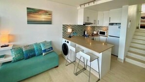Een kleine keuken met een centraal eiland, een wasmachine en een zithoek met een bank.