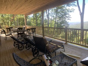 Enjoy the serene forest views from this outdoor deck, featuring comfortable seating and tables.