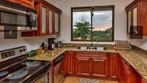 Una cocina con armarios de madera, un microondas de acero inoxidable, una estufa y un amplio ventanal con vistas al verdor.