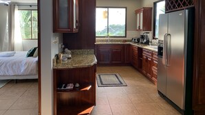 A modern kitchen with wooden cabinets, a stainless steel refrigerator, and a large window offering a view of greenery. - Chauffeur & Concierge included Luxury Jungle/Beach Pool @ Villa Tiquicia (Quepos)