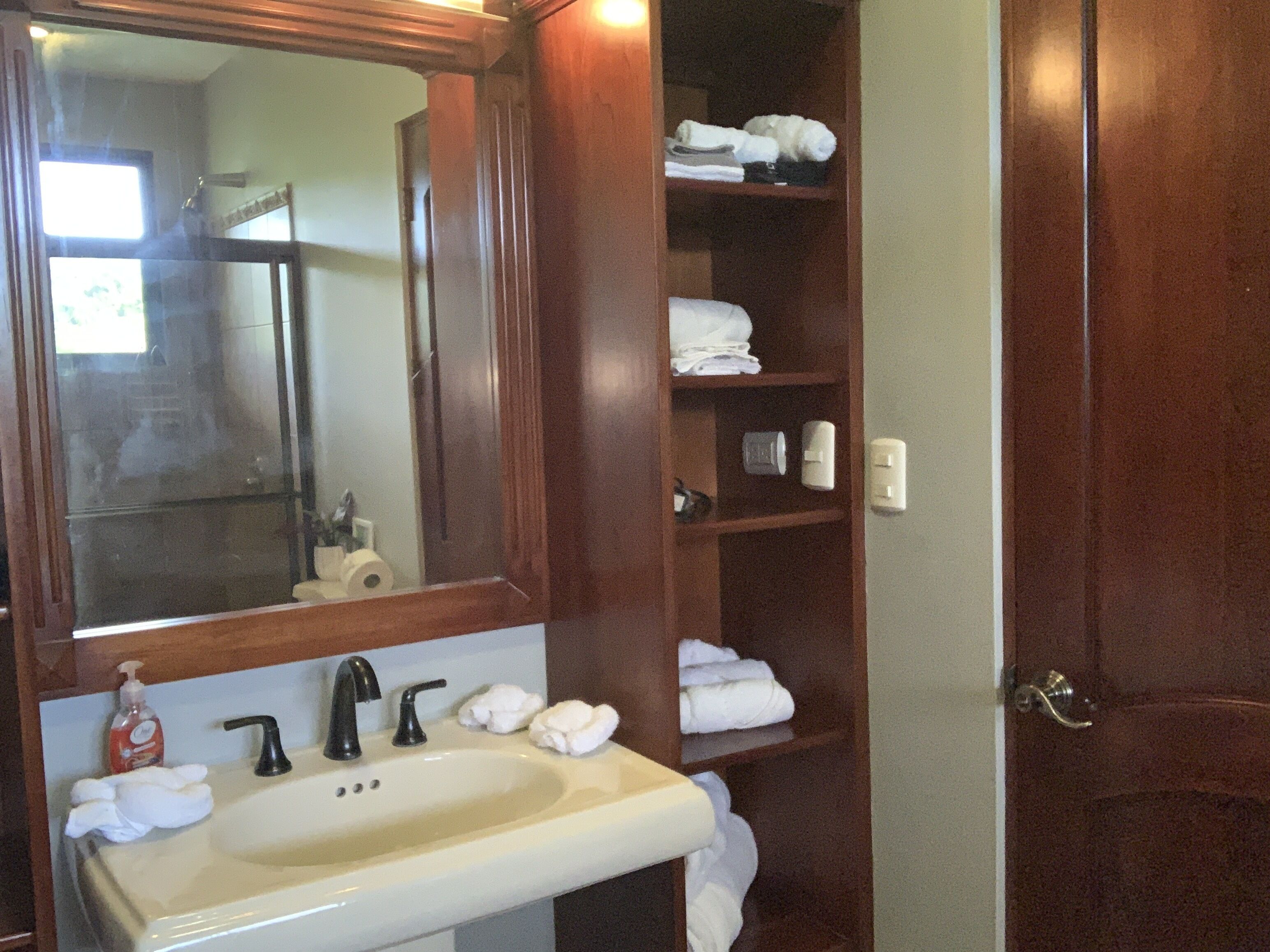 A bathroom with a sink, mirror, and shelves with towels.