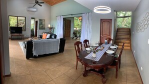 A spacious living area with a dining table set for four, a comfortable sofa, a television, and a ceiling fan. - Chauffeur & Concierge included Luxury Jungle/Beach Pool @ Villa Tiquicia (Quepos)