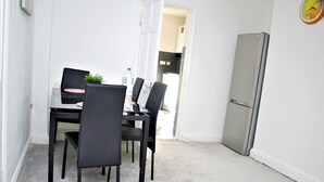 A dining area with a table and chairs, a refrigerator, and a clock on the wall. - CITY CENTRE SPACIOUS 5 BEDROOMS HOUSE AYLESBURY (Buckinghamshire)