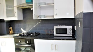 A kitchen with white cabinets, a black countertop, a stove, an oven, and a microwave. - CITY CENTRE SPACIOUS 5 BEDROOMS HOUSE AYLESBURY (Buckinghamshire)
