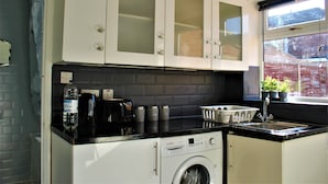 A compact kitchen with white cabinets, a Bosch washing machine, a black countertop, and a window with a view of a brick building. - CITY CENTRE SPACIOUS 5 BEDROOMS HOUSE AYLESBURY (Buckinghamshire)