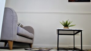 A room with a grey sofa, a small table with a plant, and a framed picture on the wall. - CITY CENTRE SPACIOUS 5 BEDROOMS HOUSE AYLESBURY (Buckinghamshire)