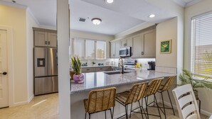 A modern kitchen with stainless steel appliances, a large island with bar stools, and a view of the outdoors. - Private townhome steps from the beach and right next to the pool (Longboat Key)