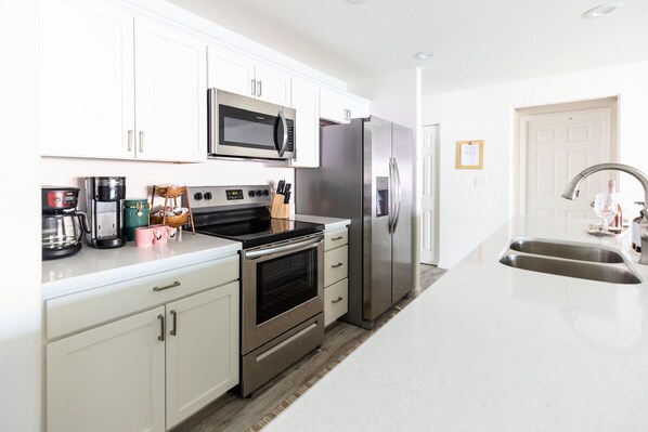Enjoy cooking in this well-equipped kitchen with stainless steel appliances, white cabinetry, and a sleek countertop.