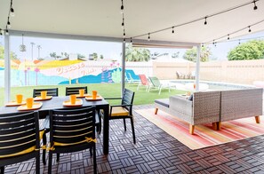 Relax in style on this inviting patio, featuring a vibrant mural and comfortable seating area overlooking the pool and lush greenery.