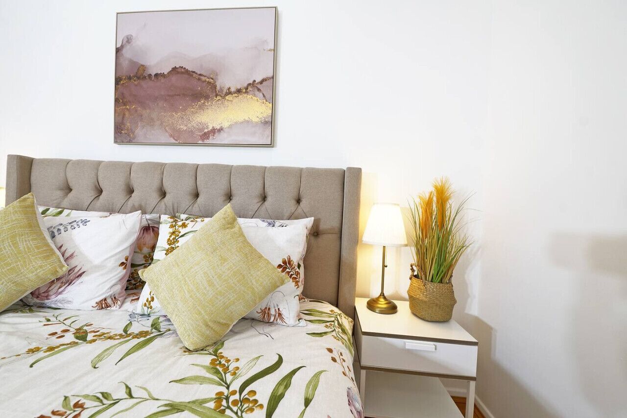 A neatly made bed with floral bedding, a tufted headboard, and a bedside lamp with a plant.