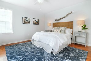 A bedroom with a bed, two bedside tables, a nightstand, a large window, and two wall-mounted pictures.