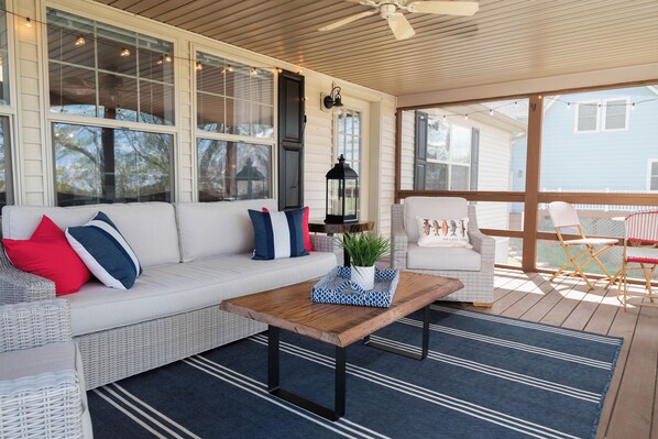 A covered porch with a white wicker sofa, a wooden coffee table, and a wicker chair.