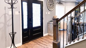 A hallway with a black door, a coat rack, a clock, and a staircase with a railing.