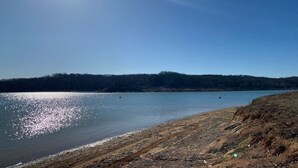 A clear view of a lake with a sandy shore and a forested hill in the background.