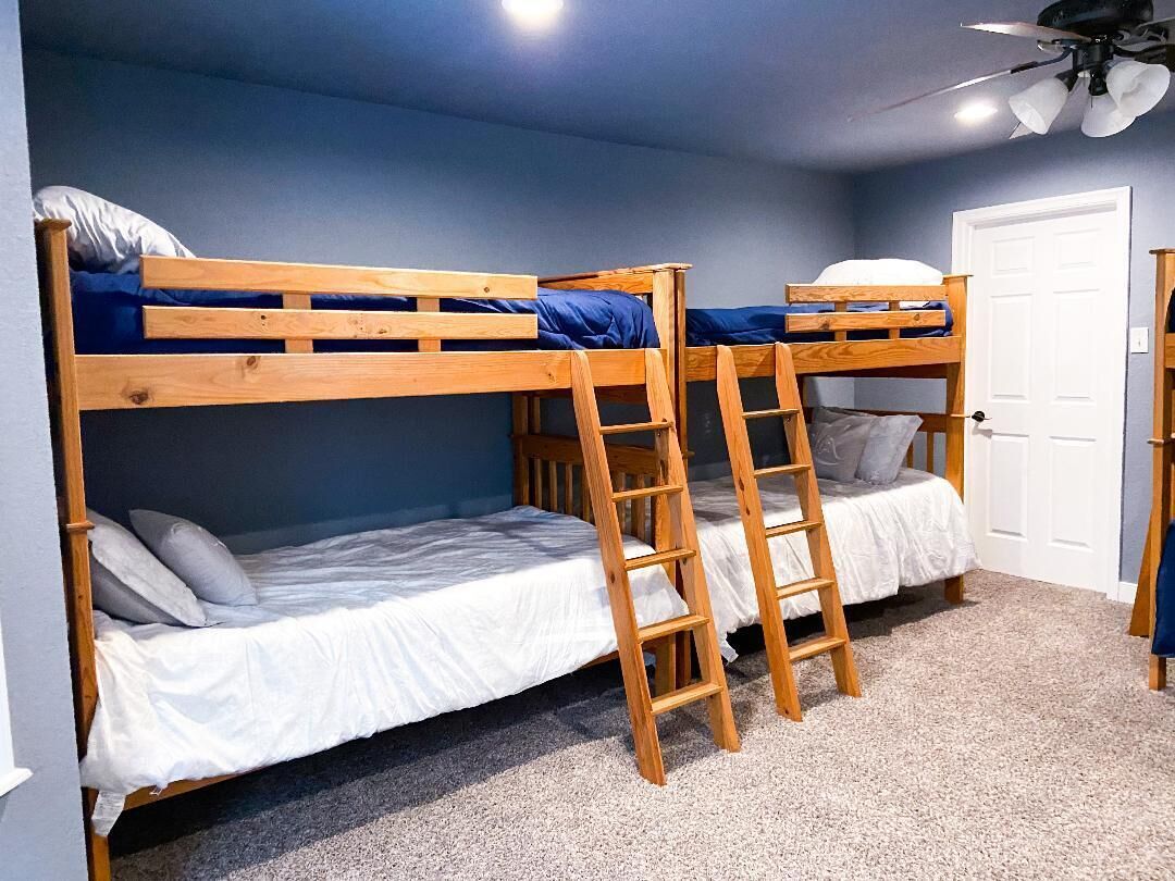A bunk bed room with a ceiling fan, a door, and a carpeted floor.