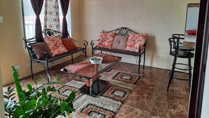 Un soggiorno con due divani in metallo nero, un tavolino in vetro, un tappeto decorato e una pianta in vaso.