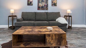 Una sala de estar con una mesa de centro de madera, un sofá gris y dos mesitas de noche con lámparas.