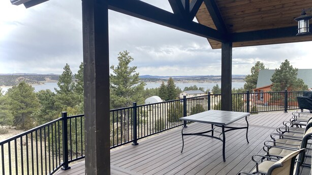 Une terrasse en bois avec une table et des chaises, d’où l’on a vue sur un lac et sur des bâtiments situés au loin.