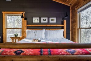 Une chambre confortable dans un chalet, avec un grand lit, une tête de lit en bois et une vue sur la forêt grâce à de grandes fenêtres.