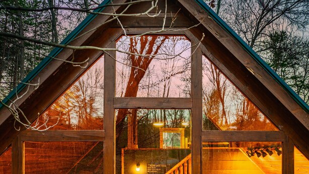 A cabin with a triangular roof, wooden walls, and a staircase leading to an upper level.