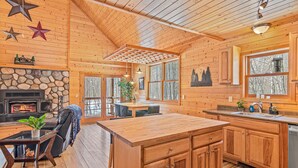 L’intérieur d’une cabane comprend une cheminée en pierre, un coin repas en bois, une cuisine avec des meubles en bois et de grandes fenêtres.