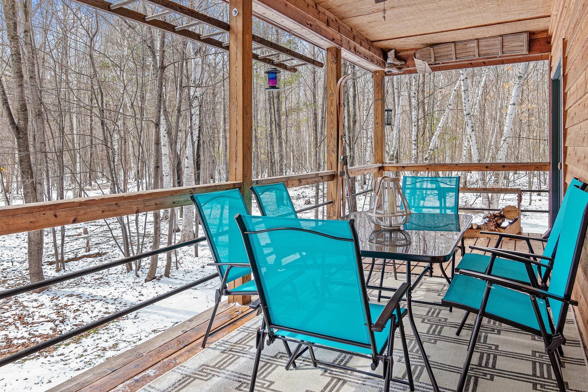 Une cabane en bois dotée d’un porche vitré, de chaises turquoise et d’une table.