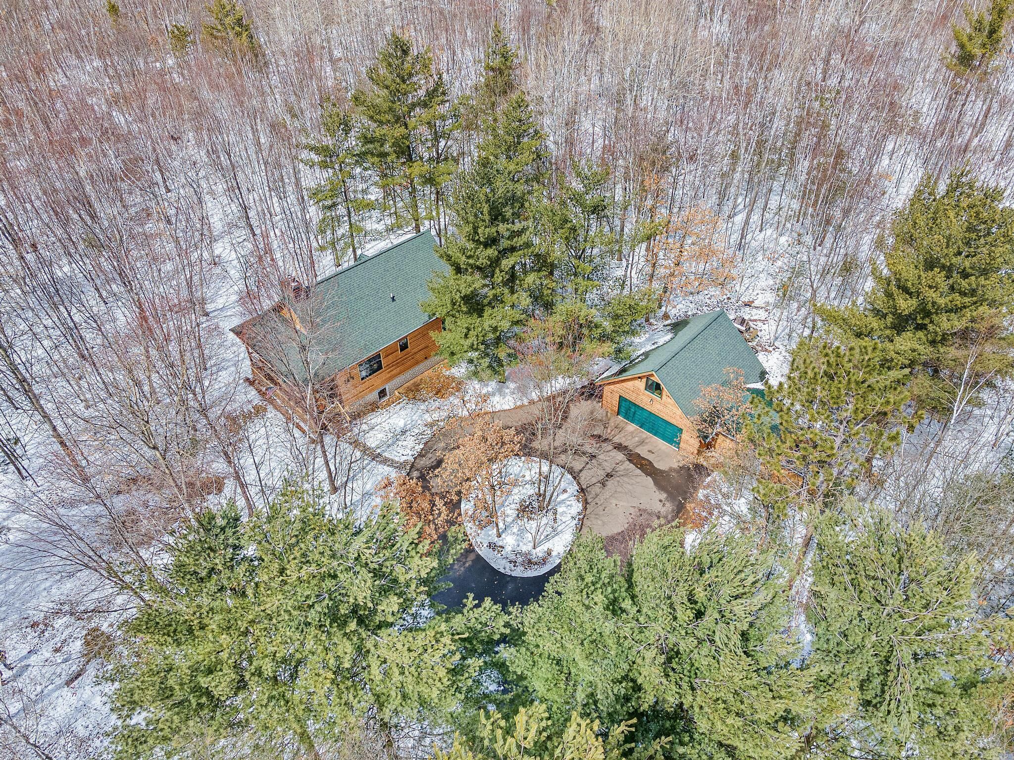 An aerial view of a cabin with a green roof, surrounded by trees and snow.