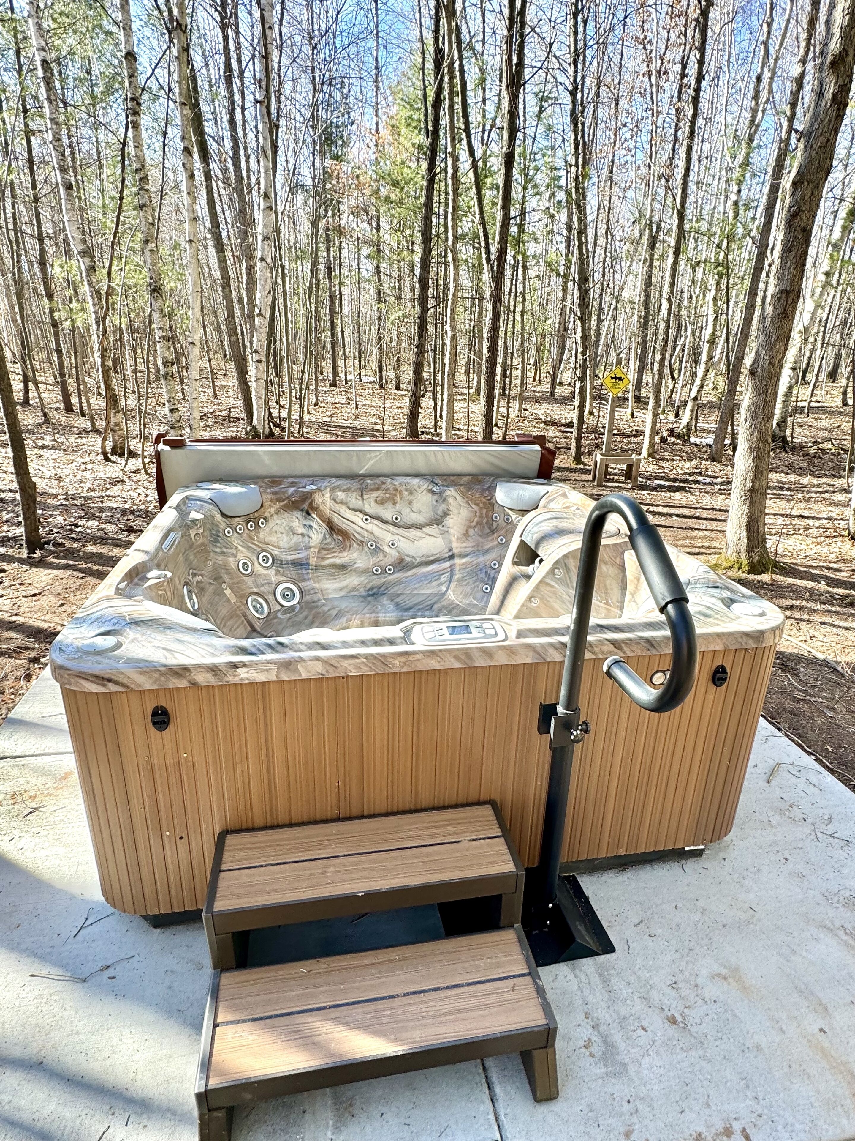Un jacuzzi con revestimiento de madera e integrado un banco, ubicado al aire libre con un bosque de fondo.