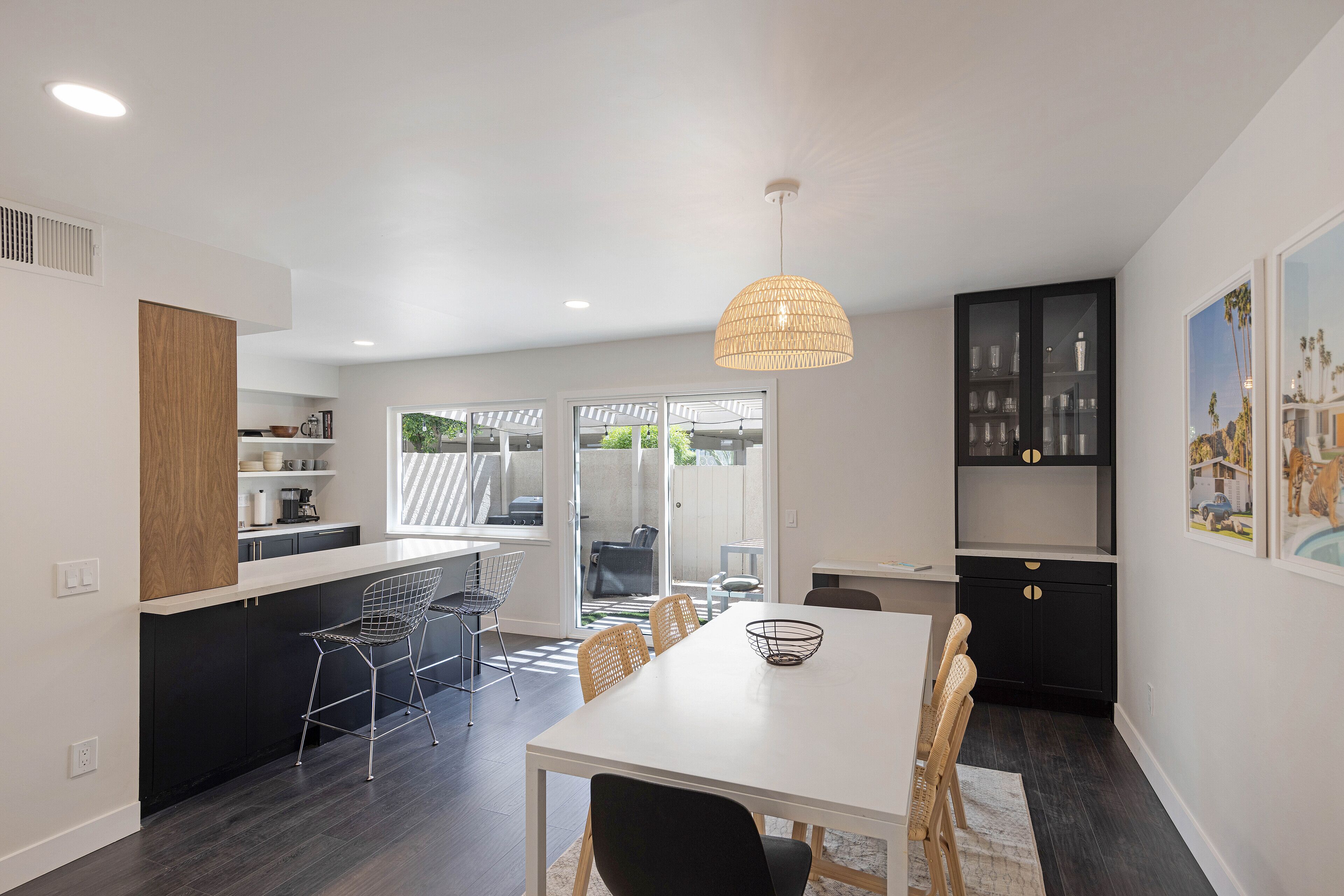 Une cuisine moderne avec un coin repas, comprenant une table blanche, des meubles de rangement noirs et un grand luminaire suspendu.