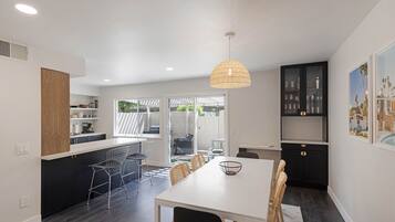Une cuisine moderne avec un coin repas, comprenant une table blanche, des meubles de rangement noirs et un grand luminaire suspendu.