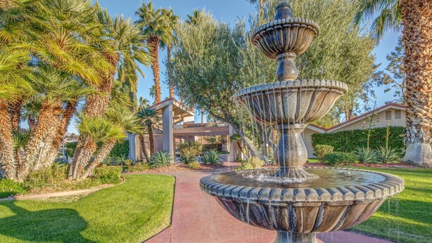 A multi-tiered stone fountain in a landscaped garden with palm trees and a pathway leading to a building. - ★Golf & Couples Oasis★ Midcentury w/6 Pools, Hot Tub (Palm Springs)