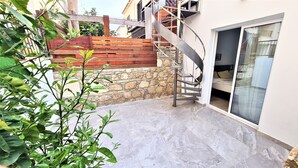 A residential area with a stone wall, a wooden fence, and a metal staircase leading to a balcony.