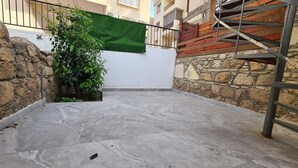 A rooftop patio with a stone wall, a green plant, and a metal staircase.