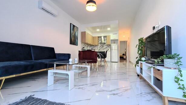 A modern living room with a black sofa, a glass coffee table, a red chair, and a TV on a white stand.