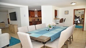 A dining area with a large wooden table, beige upholstered chairs, and a blue tablecloth.