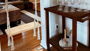 A cozy living room with a hammock, a wooden table with wine glasses, and a wall-mounted shelf with glasses. - Gentry Pines: Huge backyard ~ Loaded Game Room (Vestavia Hills)
