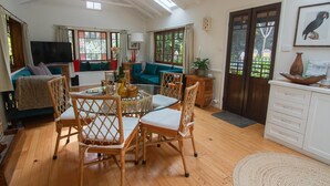 A spacious living area with a dining table, wicker chairs, a sofa, and a television.
