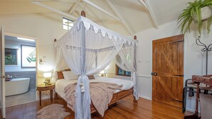 A four-poster canopy bed with a wooden frame and white drapes, a wooden door, a wooden bench, and a potted plant.