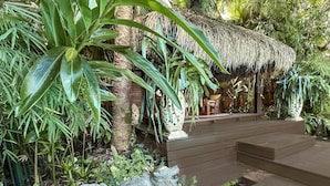 A tropical garden with a thatched-roof structure, stone steps, and lush greenery.