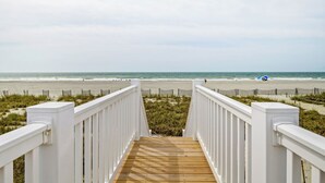 Um deck de madeira que dá para uma praia, com guarda-corpo branco em ambos os lados.